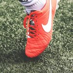 unpaired orange and white Nike soccer cleat